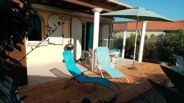 Un espacio al aire libre techado con dos sillones azules, una mesa y una sombrilla verde.