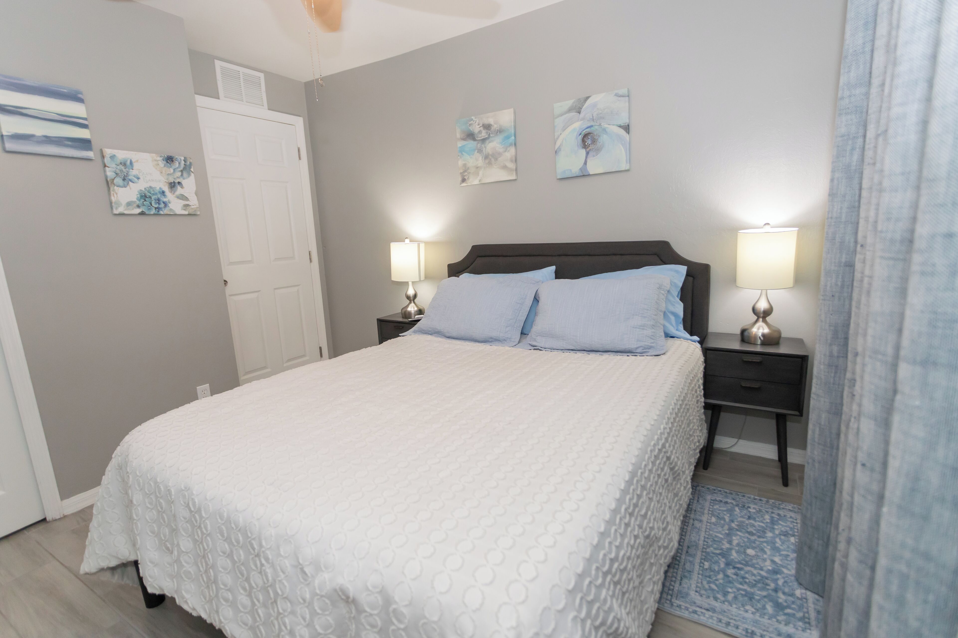 A bedroom with a bed, two bedside tables with lamps, a door, and wall art.
