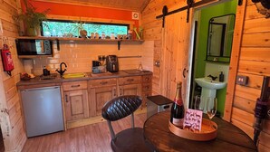 A wooden cabin interior with a dining table, chairs, a chandelier, a kitchen area with a microwave, and a sink. - Cabin, woods, hot tub, stove, coast, porch, remote, private, secure garden. (Grimston)