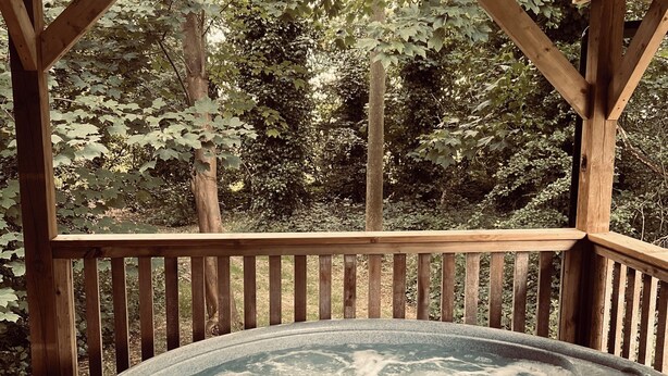 A wooden deck with a hot tub surrounded by trees. - Cabin, woods, hot tub, stove, coast, porch, remote, private, secure garden. (Grimston)