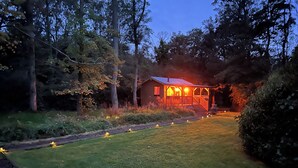 A wooden cabin with a porch, surrounded by trees and a grassy area. - Cabin, woods, hot tub, stove, coast, porch, remote, private, secure garden. (Grimston)