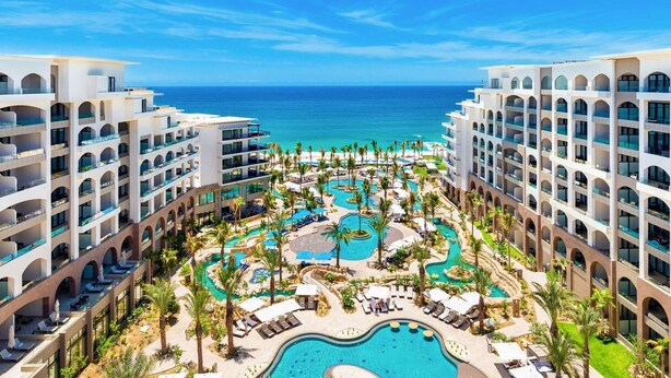 Ein Resort mit mehreren Gebäuden, einem zentralen Poolbereich und Blick auf den Ozean.