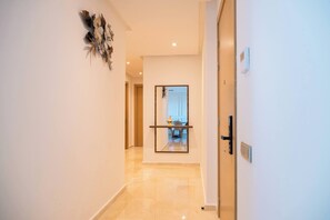 A hallway with a mirror, a door, and a wall-mounted decorative piece. - 2BR Luxury Prestigia Hay Riad Rabat (Rabat)