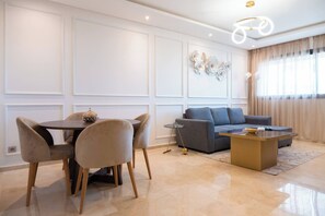 A modern living room with a dining table, chairs, a sofa, and a coffee table. - 2BR Luxury Prestigia Hay Riad Rabat (Rabat)