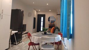A dining area with a round table, white chairs, a black refrigerator, and a blue curtain. - Iglu Beautiful apartment, two comfortable bedrooms, outdoor camera. Garden. (Villeneuve-le-Roi)