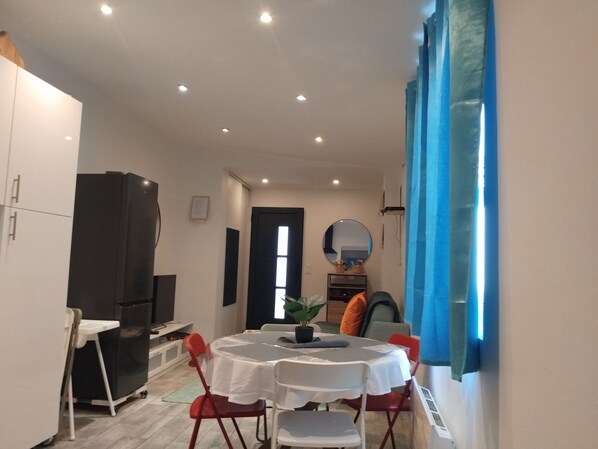 A dining area with a round table, white chairs, a black refrigerator, and a blue curtain.