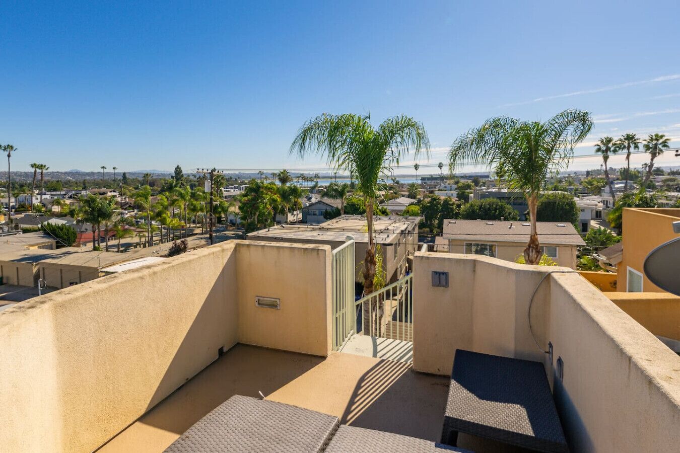 A rooftop terrace with a view of a residential area, palm trees, and a clear sky.