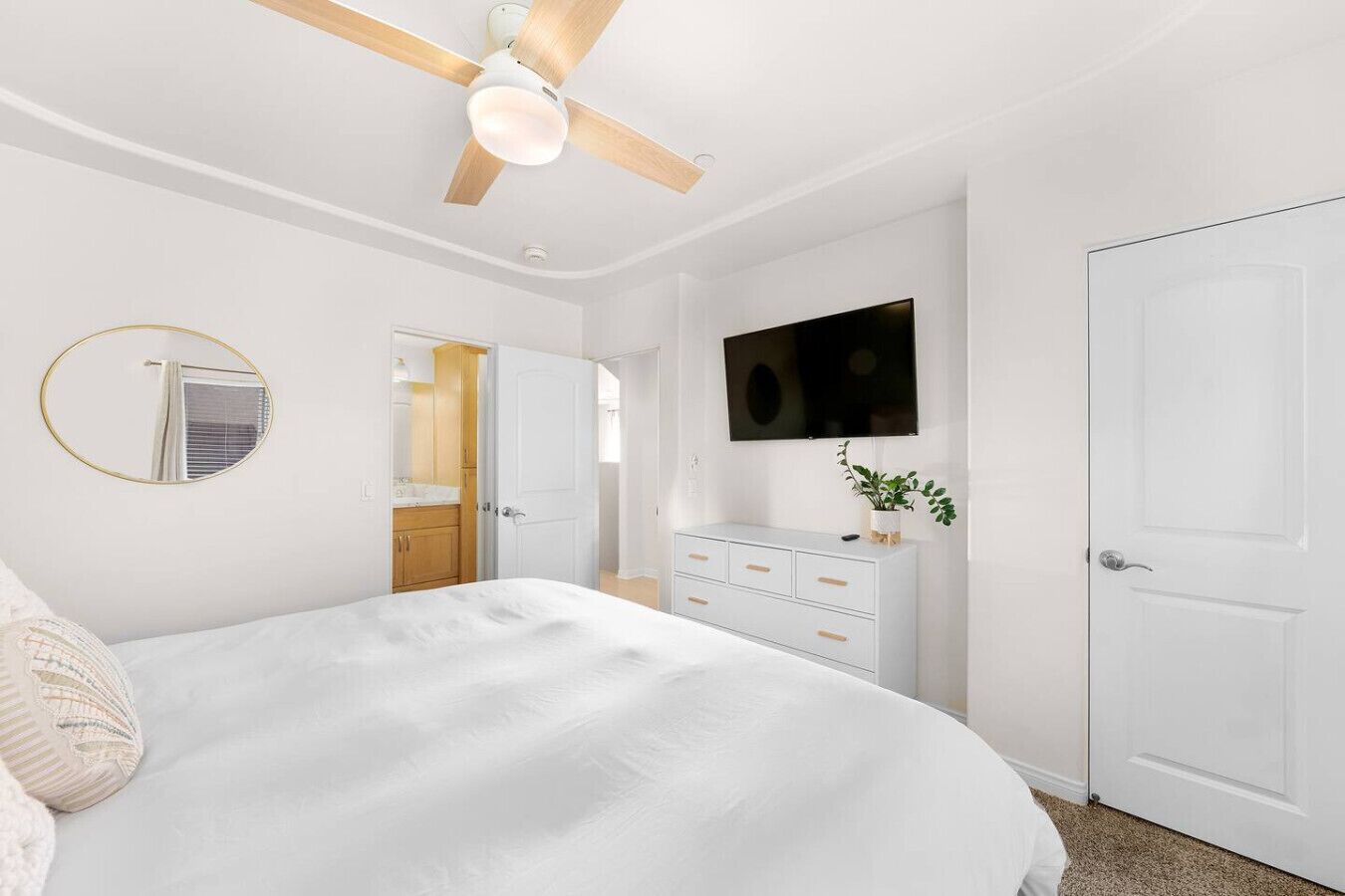 Un dormitorio con cama, ventilador de techo, televisor, cómoda y una puerta.