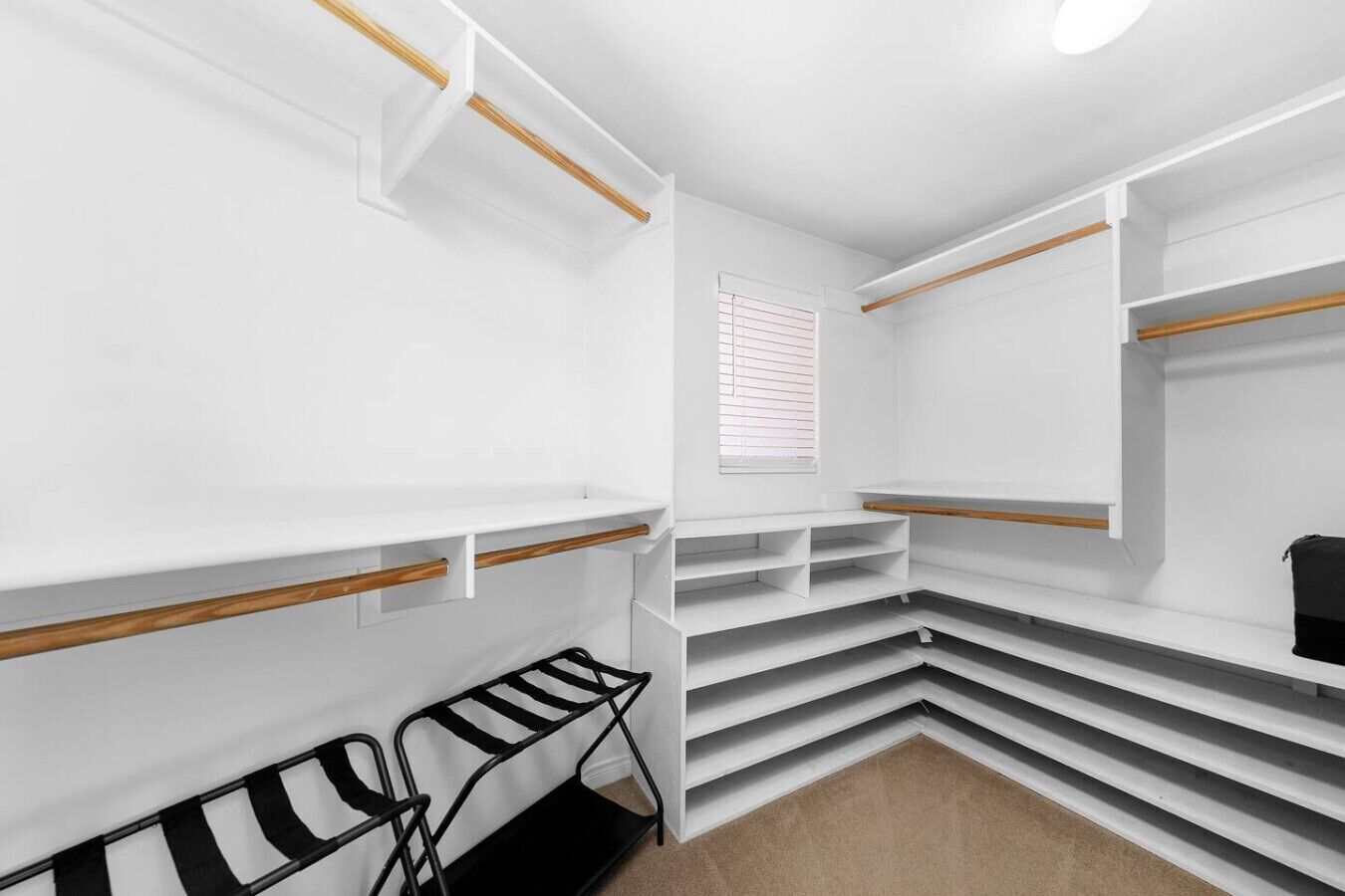 Un armario vestidor con estanterías blancas, una ventana con persianas y una silla blanco y negro.