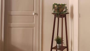 A room with a wooden floor, a white door, a small wooden stool with a potted plant, and a wall clock.