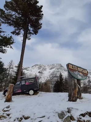 Un paysage de montagne avec un panneau indiquant « RE STO-MONTAGNE » et un véhicule portant l’inscription « La Lucette BAR-RESTAURANT ».