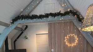 A cozy loft bedroom with a sloped ceiling, a built-in heater, a comfortable chair, a bed with a patterned bedspread, and a decorative wall with vertical wooden slats and string lights. - Chalet 2 bedroms 2-6 person (Campan)