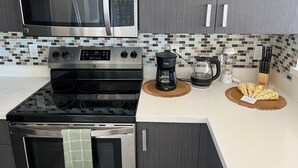 Ett modernt kök med en mikrovågsugn i rostfritt stål, en svart spis, en kaffebryggare och en vattenkokare på bänkskivan.