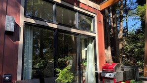 Un edificio moderno con amplios ventanales, una parrilla y mobiliario para exterior.