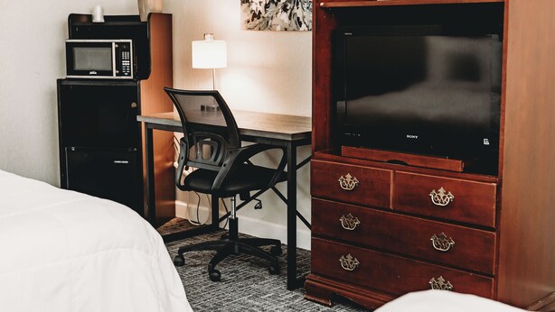 Une chambre d’hôtel comprenant un lit, un bureau avec une chaise, un four à micro-ondes, une commode et un téléviseur.