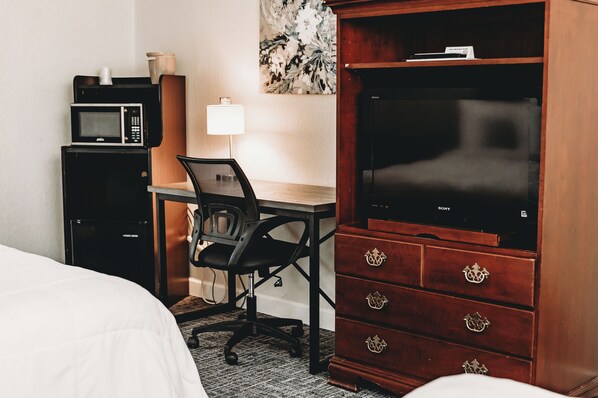 Une chambre d’hôtel comprenant un lit, un bureau avec une chaise, un four à micro-ondes, une commode et un téléviseur.