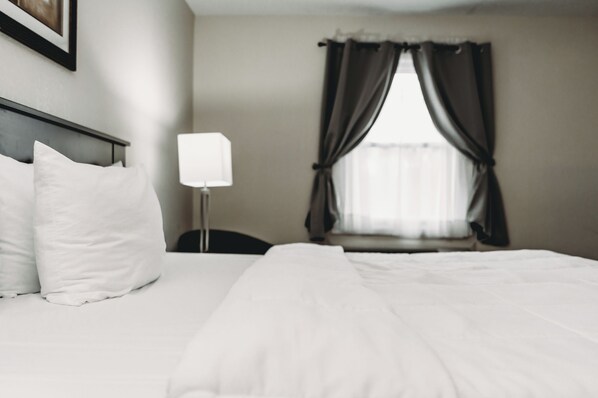 Une chambre d’hôtel avec un lit, une table de chevet, une lampe et une fenêtre avec des rideaux.