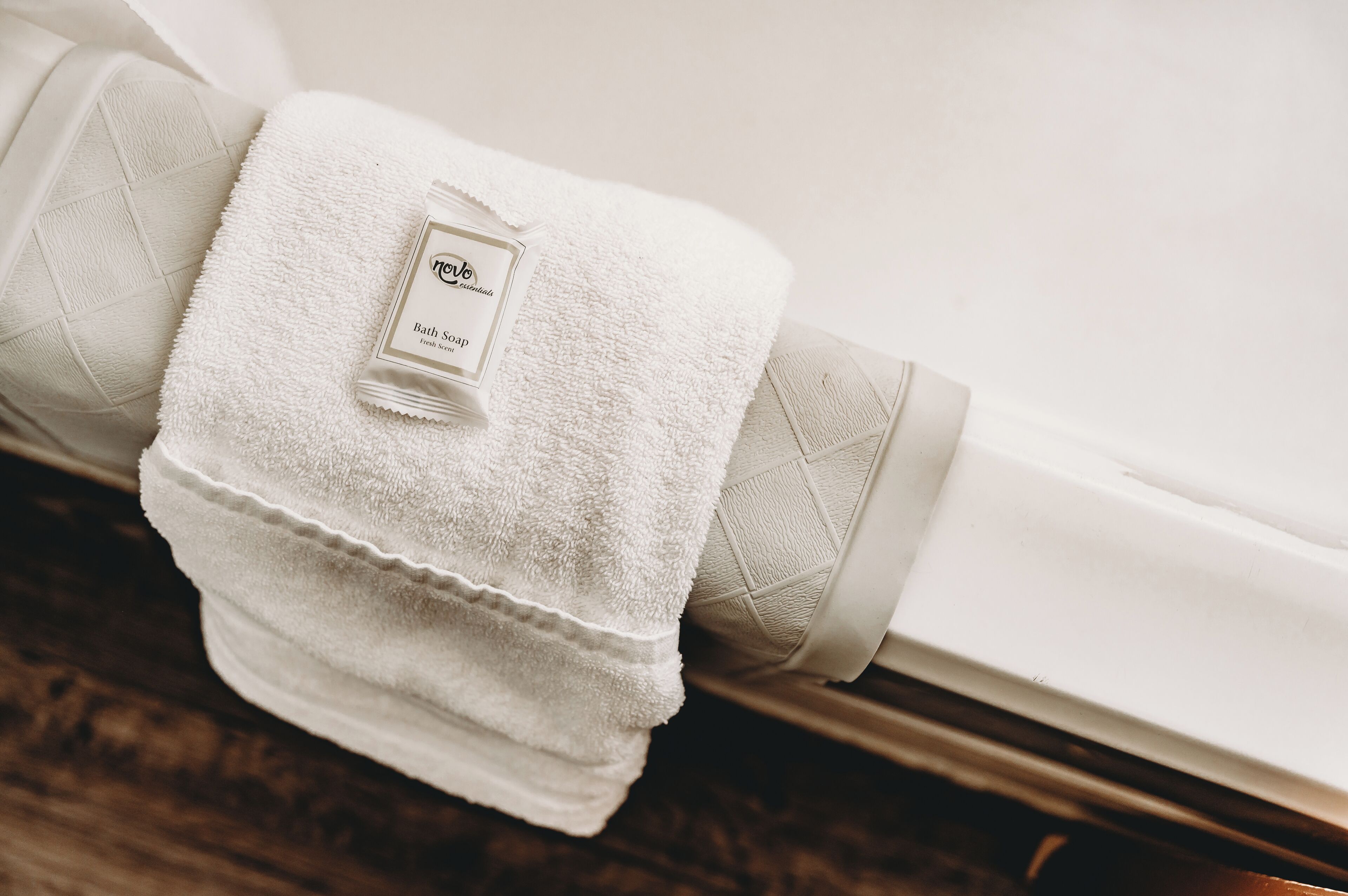 A neatly folded white bath towel with a bottle of bath soap placed on top, resting against a white bathtub.