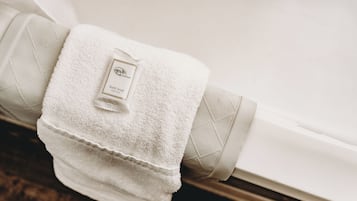 Une serviette de bain blanche, soigneusement pliée, est posée sur une bouteille de savon pour le bain, le tout reposant contre une baignoire blanche.