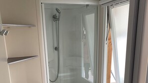 Une salle de bain compacte dotée d’une cabine de douche, d’un meuble-lavabo intégré avec des tiroirs et d’une fenêtre.