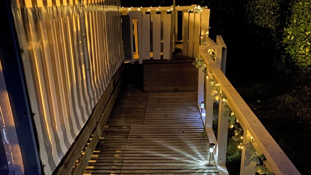 Une terrasse en bois, dotée de rampes et illuminée de guirlandes lumineuses.