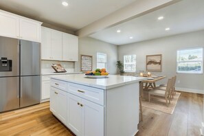 A modern kitchen with white cabinetry, a stainless steel refrigerator, a central island with a fruit bowl, and a dining area with a wooden table and chairs. - Walking distance to City of Hope -Bright 4BR -Private Patio Outdoor Living (Duarte)