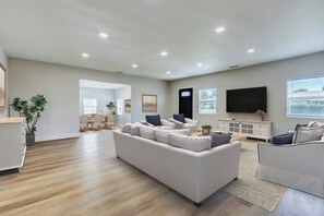 A spacious living room with a large sofa, a television, and a dining area in the background. - Walking distance to City of Hope -Bright 4BR -Private Patio Outdoor Living (Duarte)