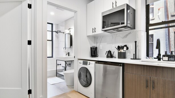 A modern kitchen with a washing machine, microwave, and wooden cabinets. - 1 Bedroom New Renovated - Wash/Dryer & Kitchenette -E (New York)