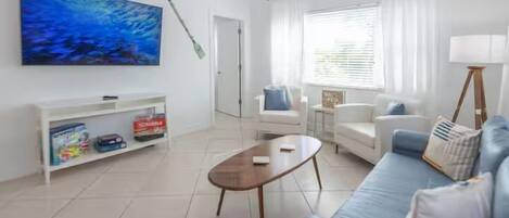 Una sala de estar con sofá, mesa de centro, televisor y estantería.