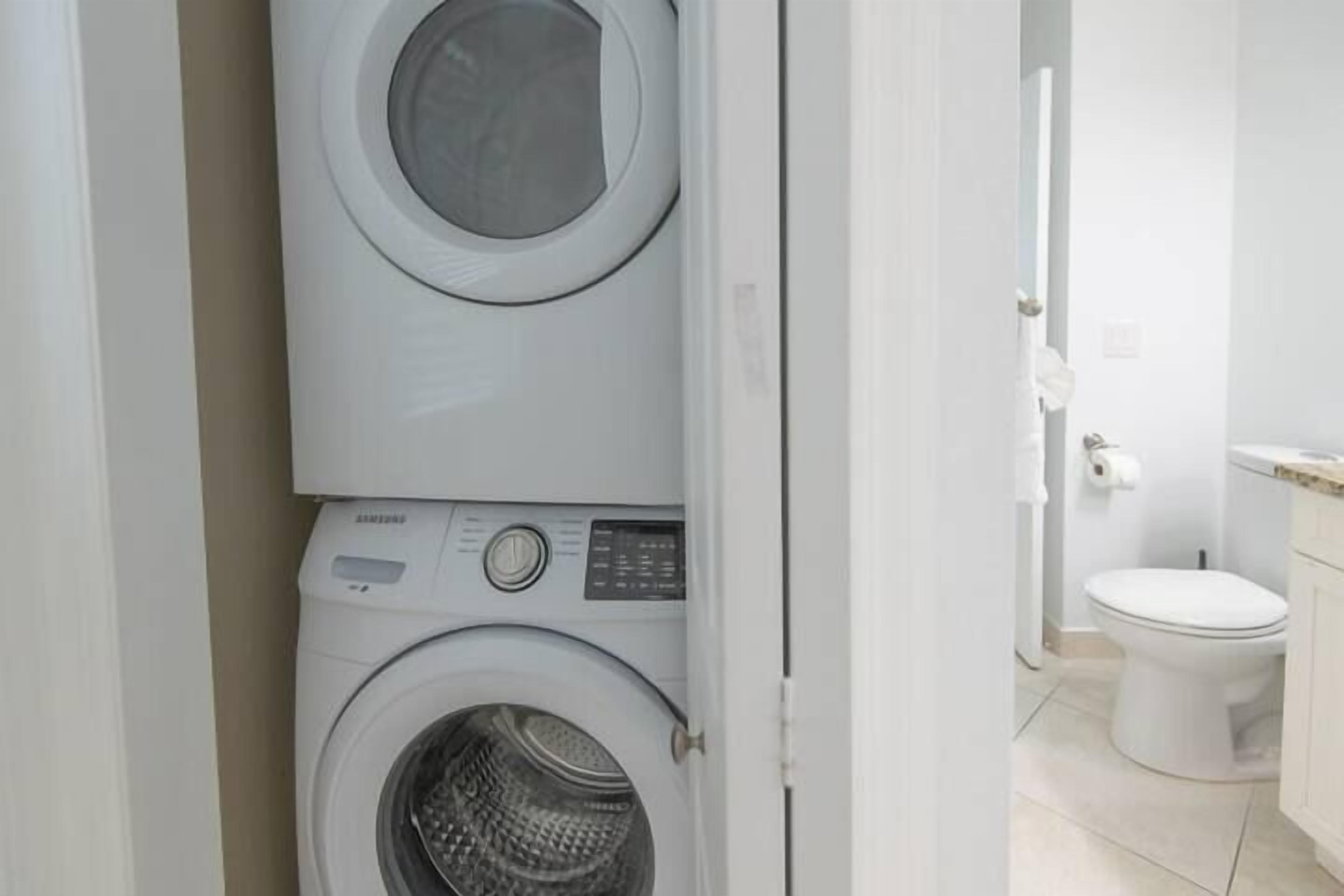 A laundry room with stacked appliances, a toilet, and a sink.