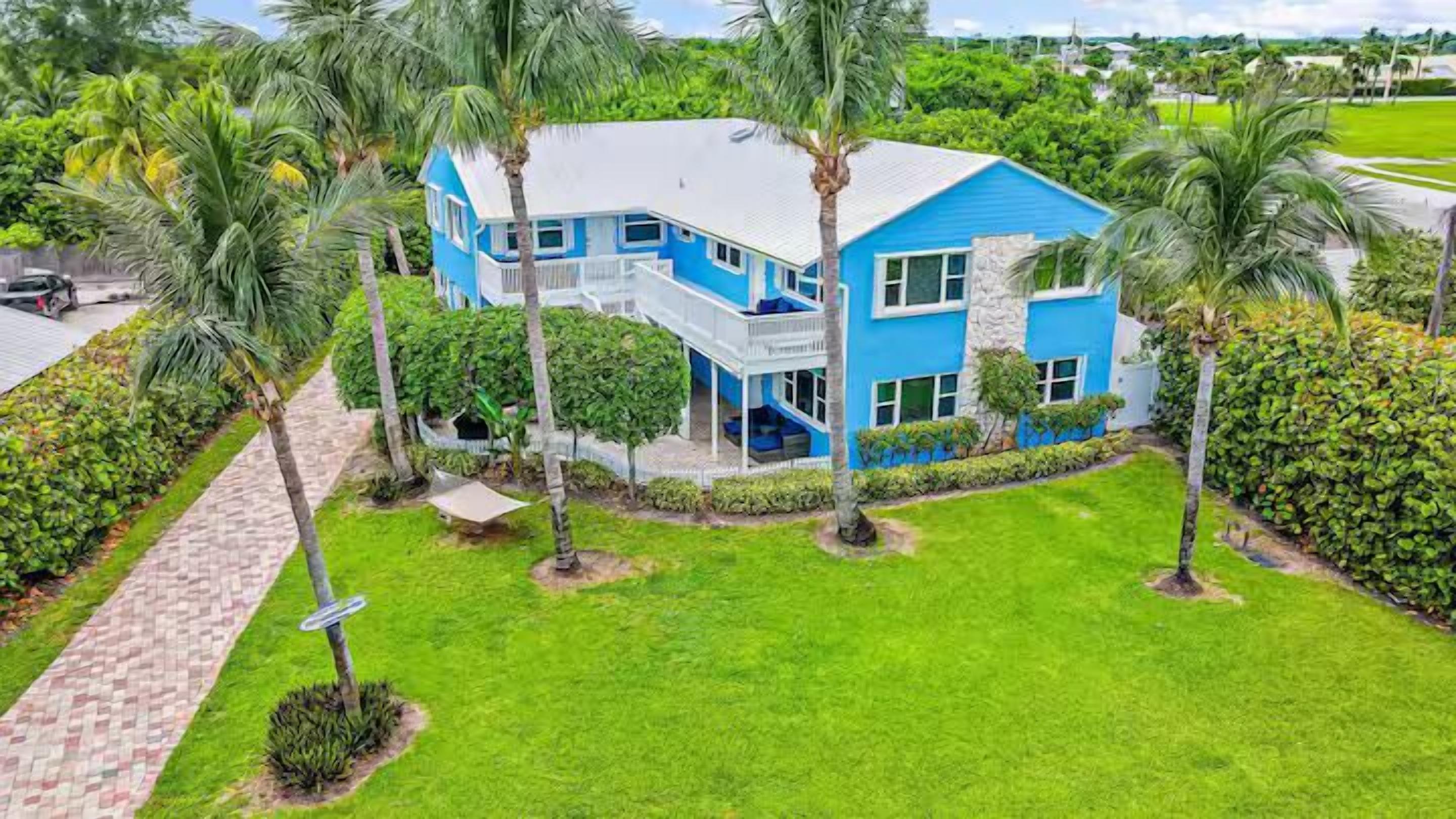 A two-story house with a blue exterior, surrounded by a well-maintained lawn and palm trees.
