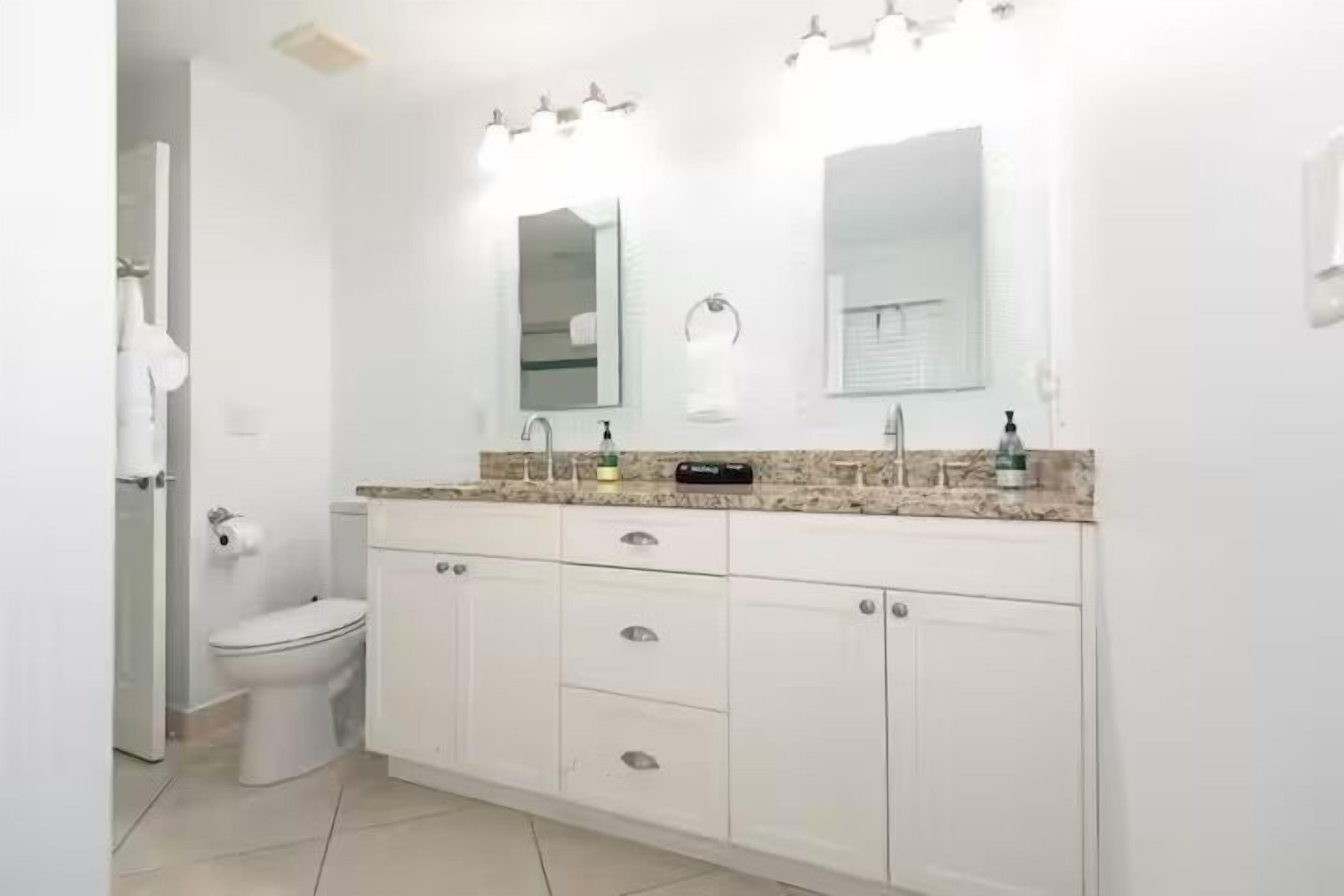 Une salle de bain avec des toilettes blanches, un lavabo avec un miroir et des placards.