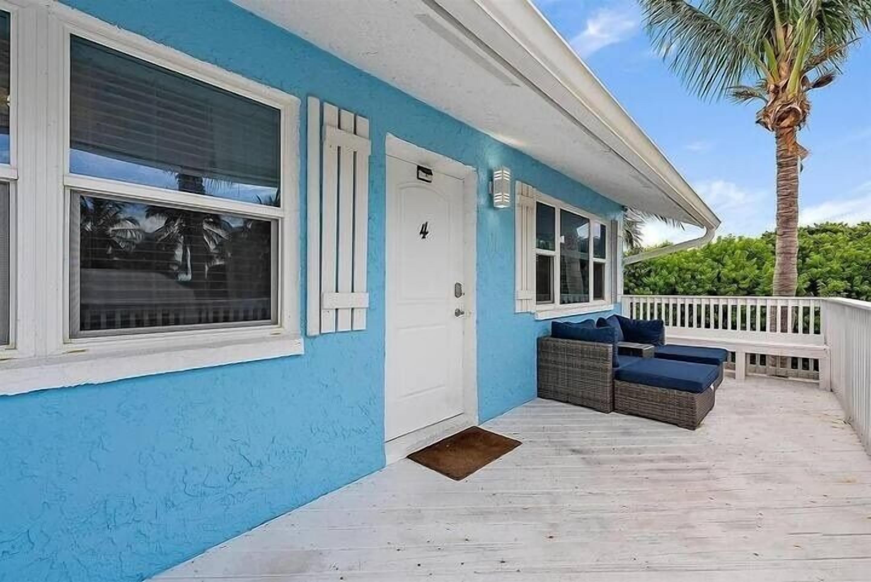 Une maison à l’extérieur bleue, avec une porte blanche et un porche meublé de meubles en osier.