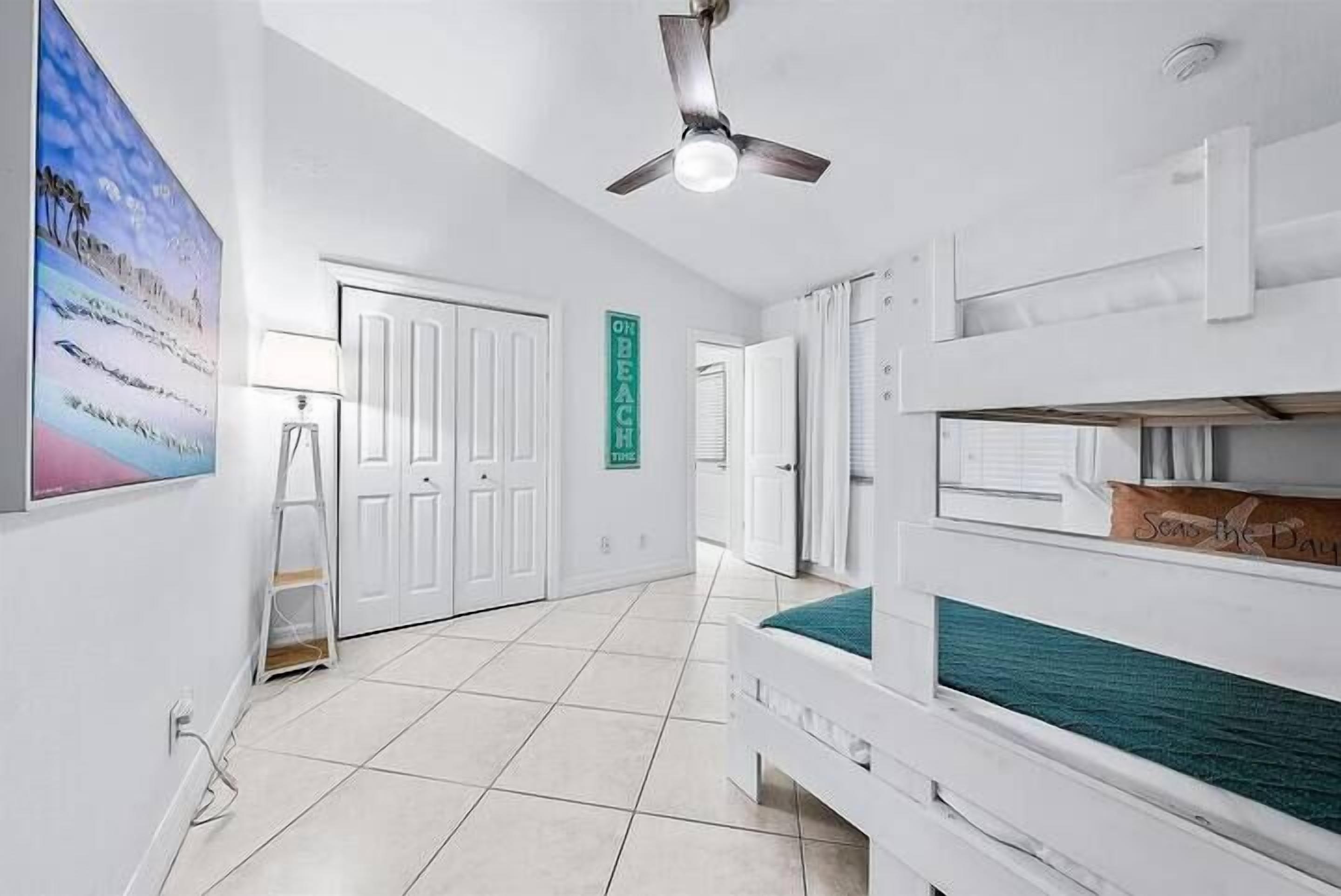 A room with bunk beds, a ceiling fan, a white door, and a framed picture on the wall.