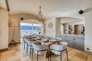Un espace repas avec une longue table dressée pour six personnes, un lustre et une vue sur l’extérieur.