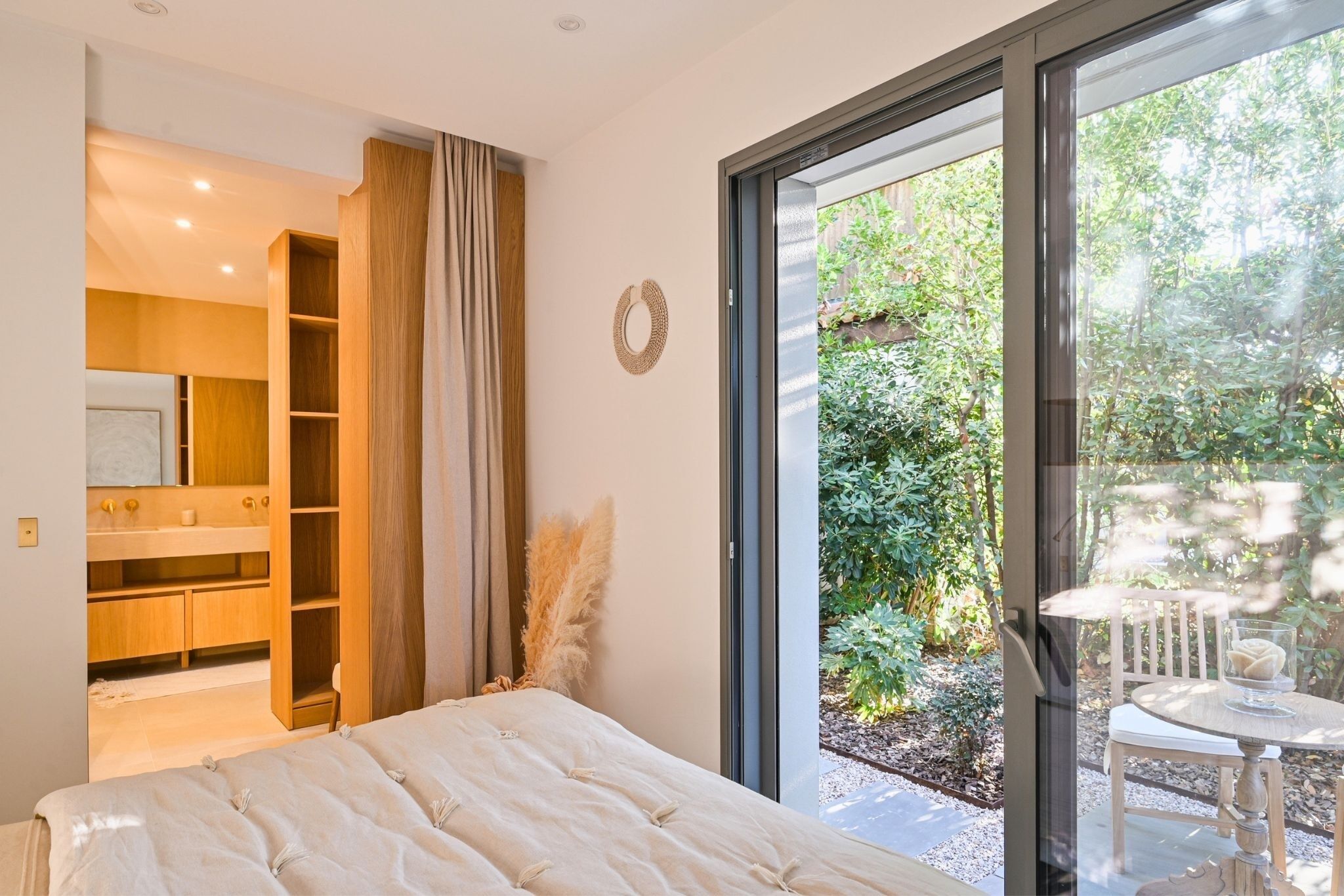 Un dormitorio con una cama grande, armario empotrado, baño y puerta corredera de cristal que da a un jardín.