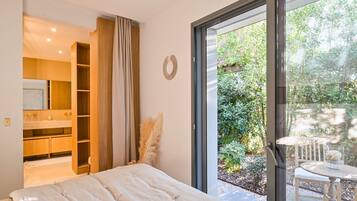 Un dormitorio con una cama grande, armario empotrado, baño y puerta corredera de cristal que da a un jardín.