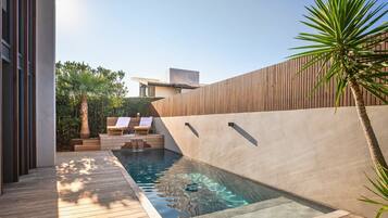 Un área de piscina moderna al aire libre con cubierta de madera, sillas de descanso y un muro de madera.