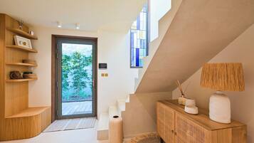 Un interior moderno con una escalera de madera, un aparador con objetos decorativos y un ventanal con vistas al verdor.