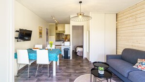 A modern living room with a sofa, a dining table with chairs, a TV mounted on the wall, and a kitchen area in the background. - Le Patio de Bénodet - avec parking (Benodet)