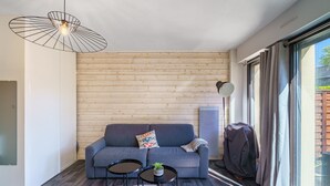 A modern living room with a grey sofa, two small round tables, a hanging light fixture, and a large window with curtains. - Le Patio de Bénodet - avec parking (Benodet)