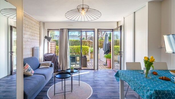 A modern living room with a sofa, a round table, a dining table with a blue tablecloth, and a ceiling light fixture. - Le Patio de Bénodet - avec parking (Benodet)