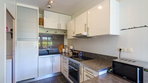 A modern kitchen with white cabinets, a built-in oven, a microwave, and a window overlooking a garden. - Le Patio de Bénodet - avec parking (Benodet)