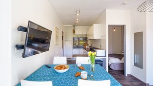 A modern hotel room with a dining area, a TV mounted on the wall, a kitchen area, and a bed with a view. - Le Patio de Bénodet - avec parking (Benodet)
