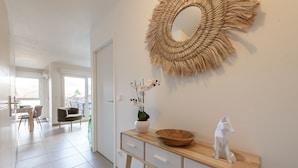 A modern interior with a wooden console table, a woven mirror, and a vase with flowers. - Le Cocon Élégance - à 500m du lac (Duingt)