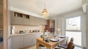 A modern kitchen with wooden cabinets, a dining table with chairs, and a pendant light. - Le Cocon Élégance - à 500m du lac (Duingt)