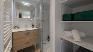 A modern bathroom with a glass-enclosed shower, a vanity with a mirror, and a shelf with folded towels. - Le Cocon Élégance - à 500m du lac (Duingt)