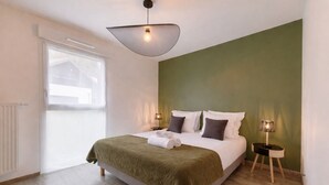 A bedroom with a bed, two bedside lamps, a window, and a radiator. - Le Cocon Élégance - à 500m du lac (Duingt)