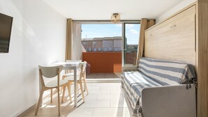 Ein kleiner, heller Raum mit Balkon, einer Couch, einem Tisch und Stühlen.