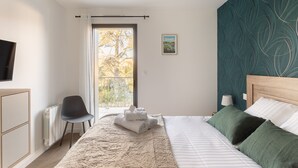 Ein Schlafzimmer mit Bett, Sessel, Heizkörper, Fernseher, Fenster mit Blick und einer Wand mit Muster.